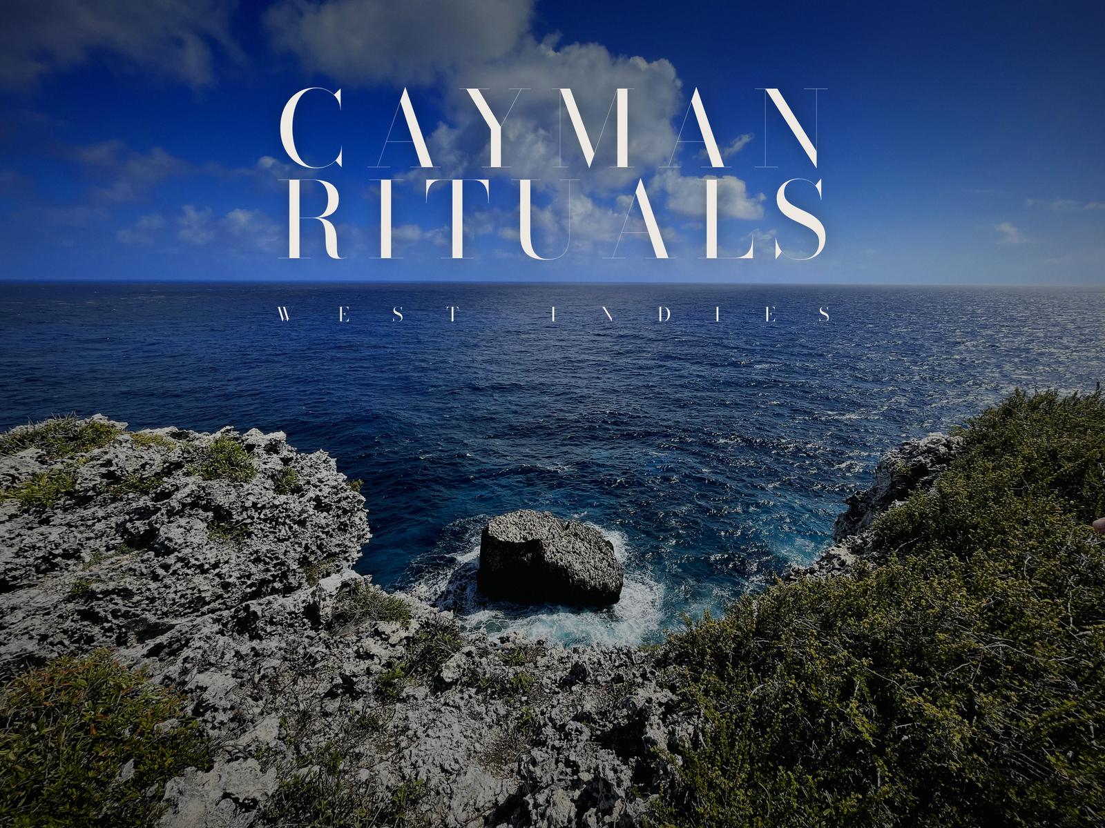 Cayman Rituals, West Indies: the wordmark over the view from the top of the Bluff on Cayman Brac, with the horizon between the two lines. Grey ironshore and low scrub in the foreground, a rock islet in white water below, and open blue sea to the horizon under a sky of small clouds.