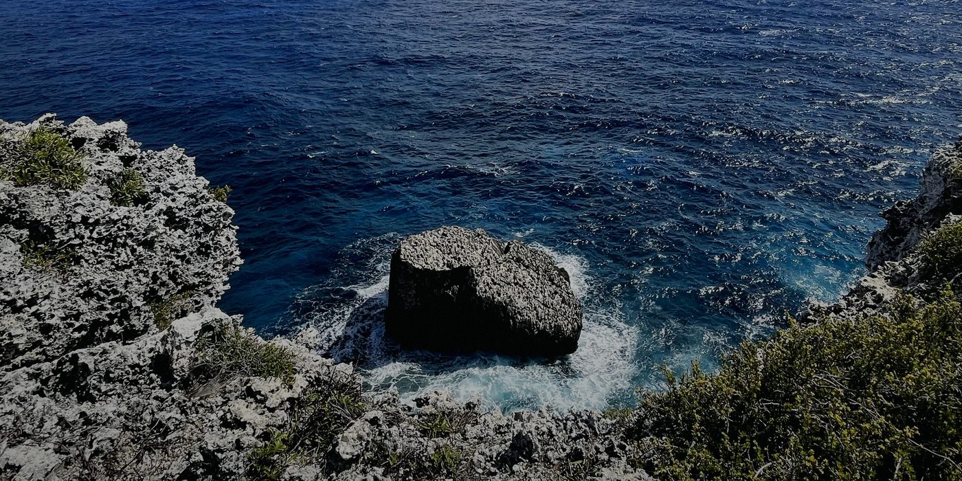 Dark sea breaking white around a rock islet, seen from the top of the Bluff on Cayman Brac.